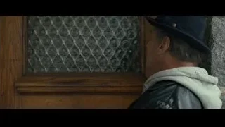 elderly man leaning against wooden door — Creed 2